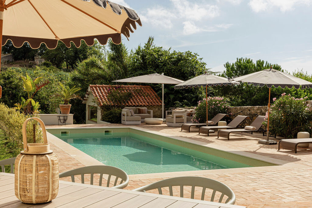 Scalloped cream parasol and wicker lantern beside the pool, tiled pool house behind