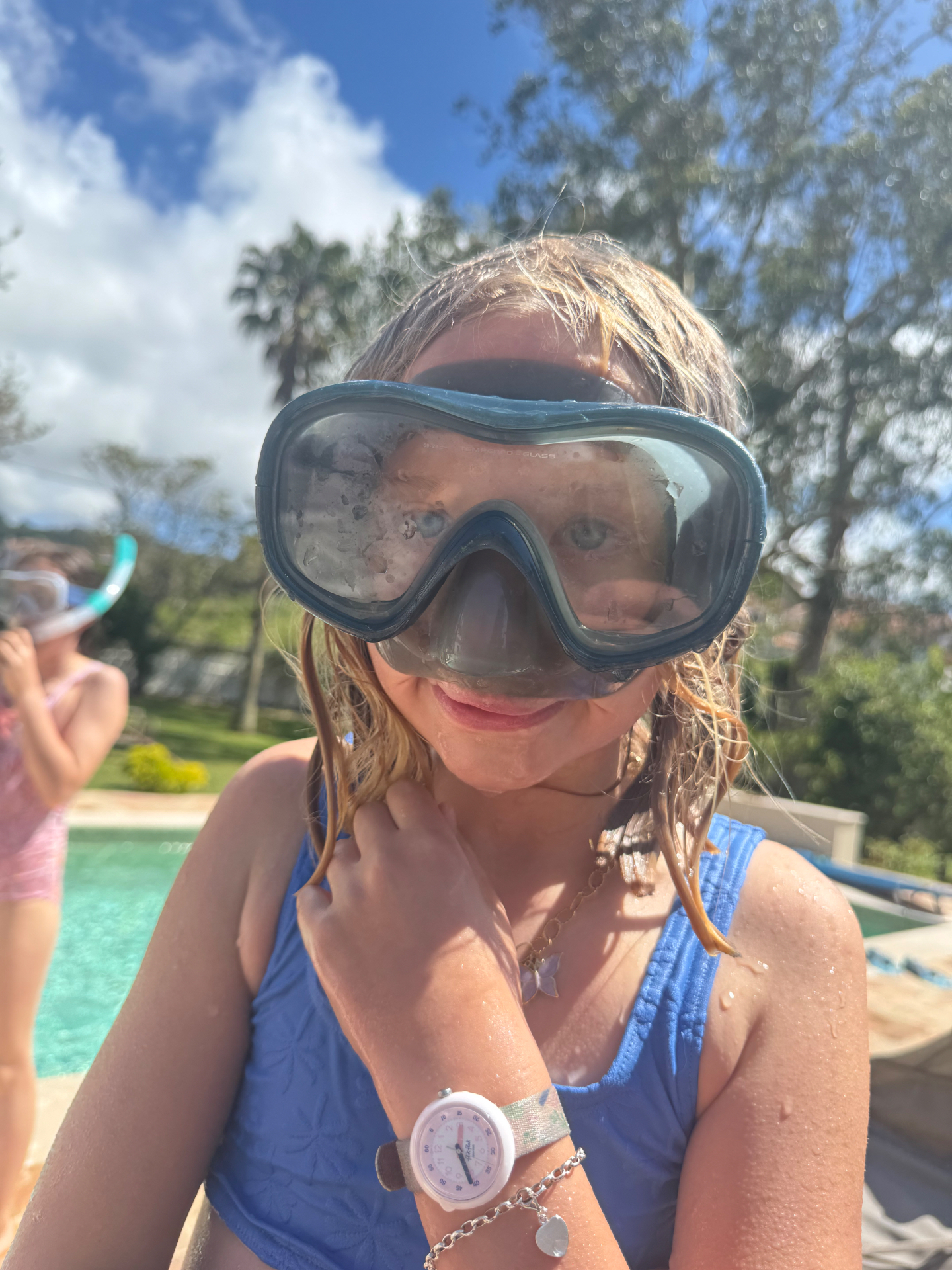 A child in a blue swimsuit and snorkel mask smiling by the pool