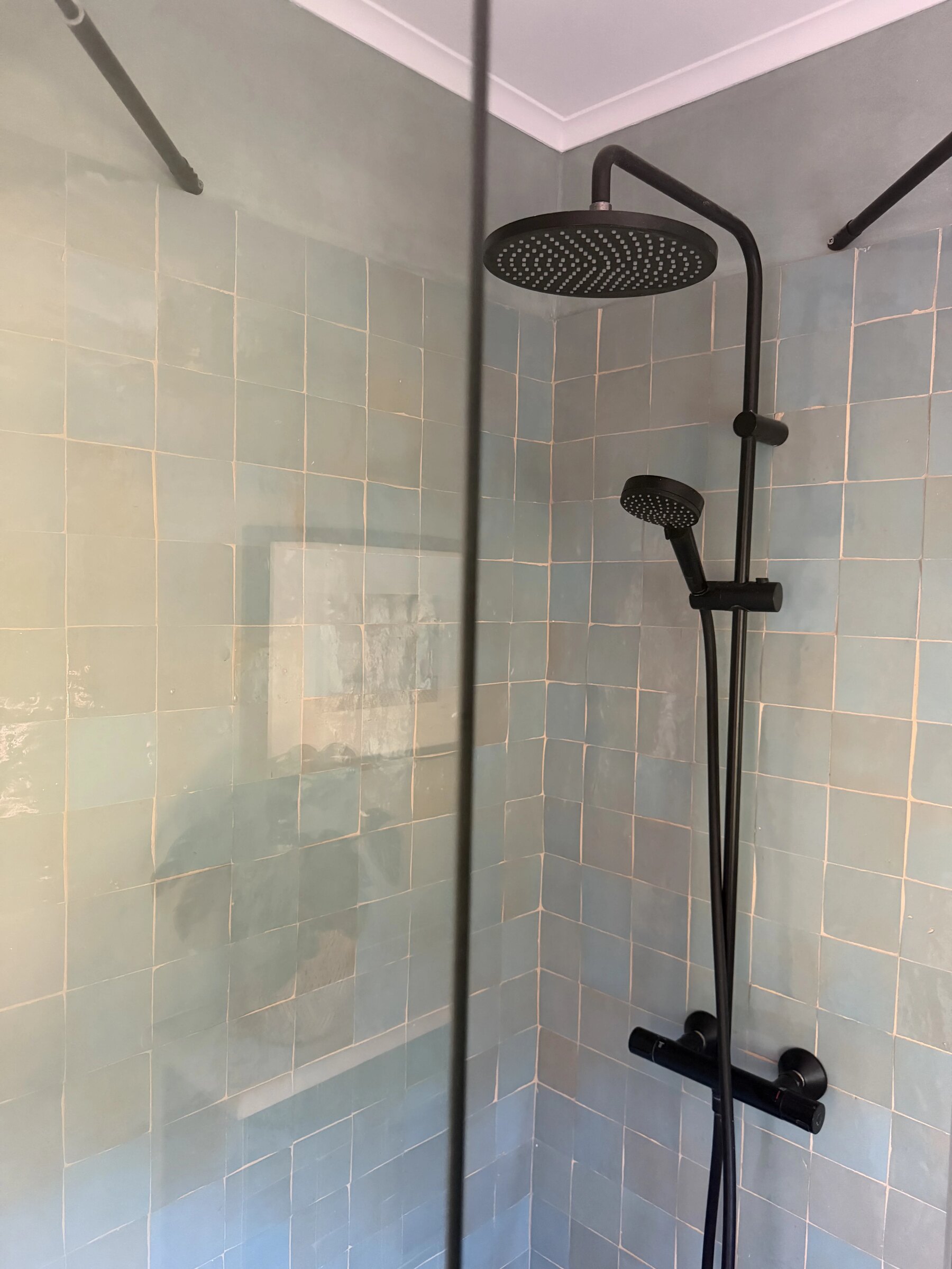 Shower in pale green zellige with a black rain shower head