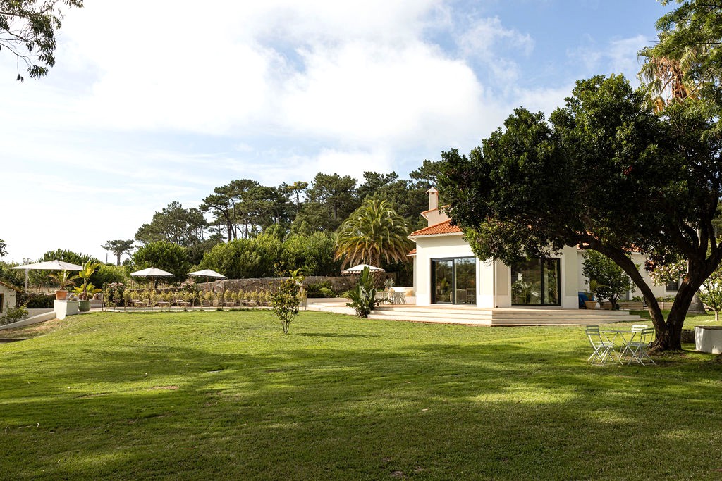 The white house with terracotta roof across a broad green lawn, umbrellas set out on the terrace
