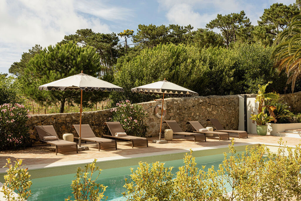 Sun-loungers under cream parasols on the stone terrace beside the pool