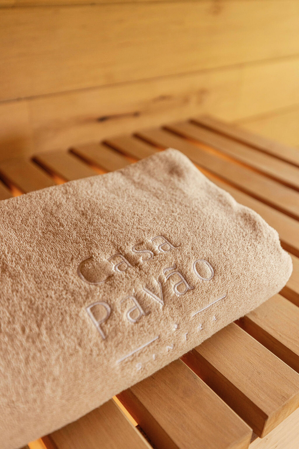A folded towel embossed Casa Pavão resting on a pale wood sauna bench