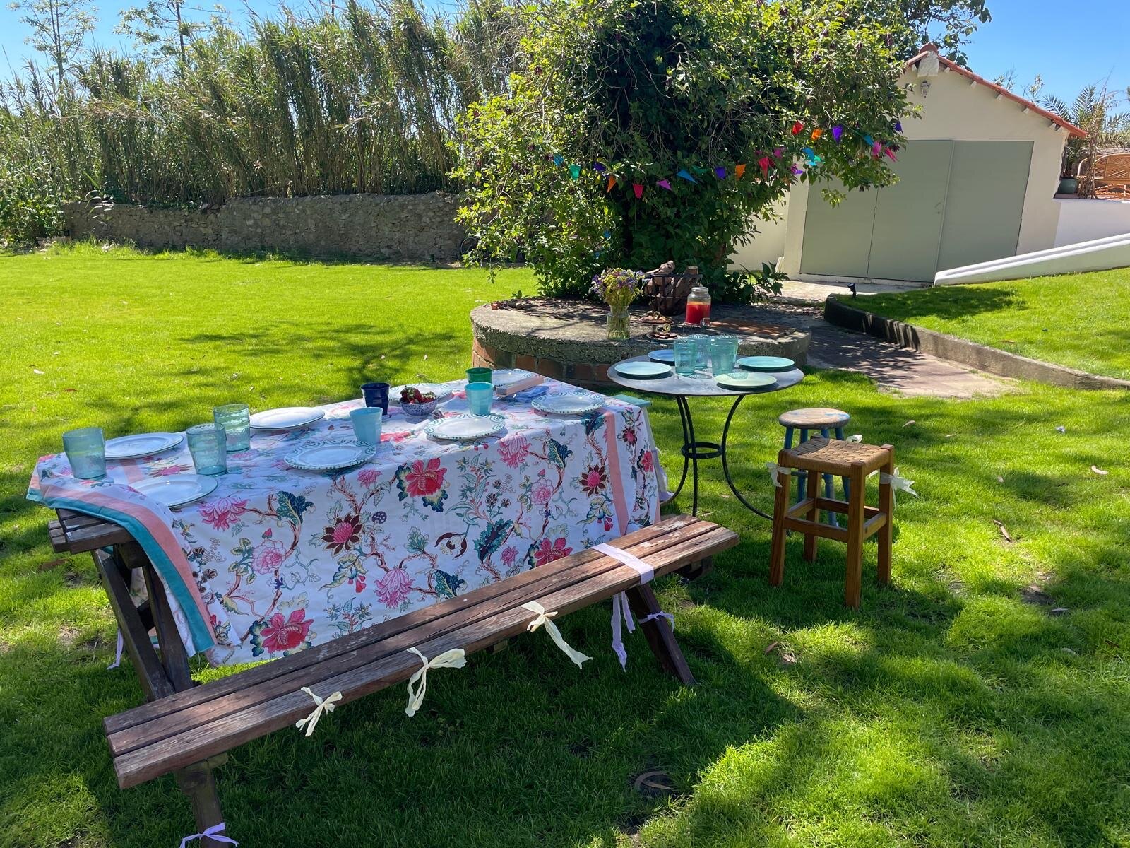 Long table on the lawn dressed with a floral cloth and stools