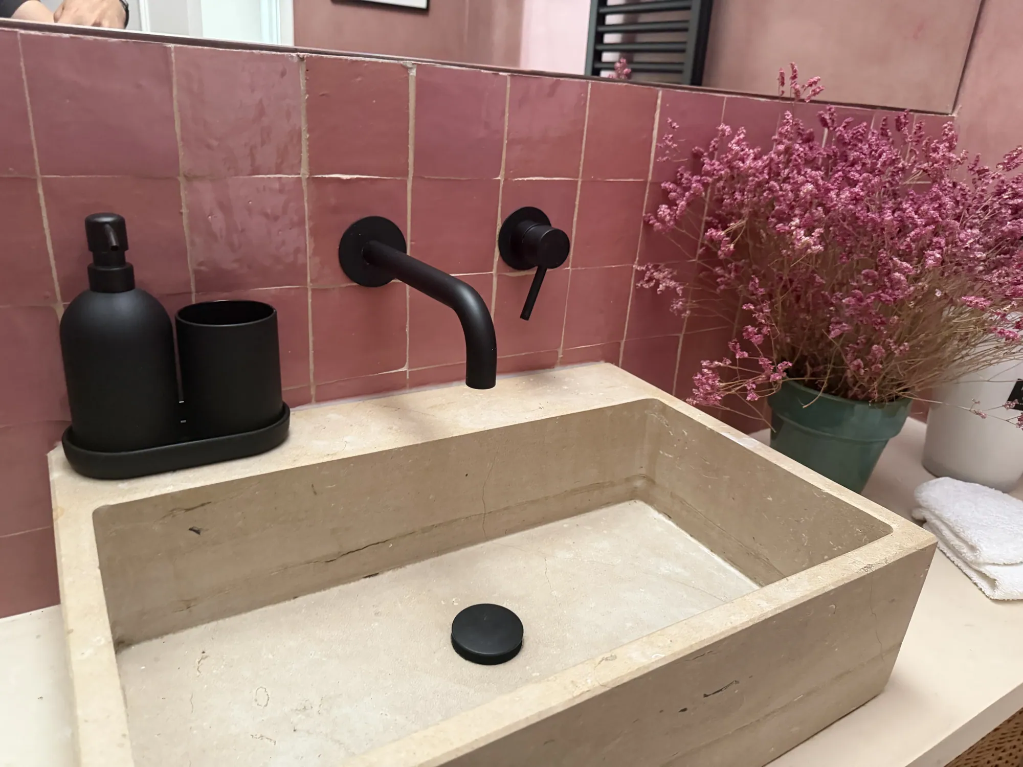 Pink zellige bathroom with a carved stone basin, black tap and dried pink flowers