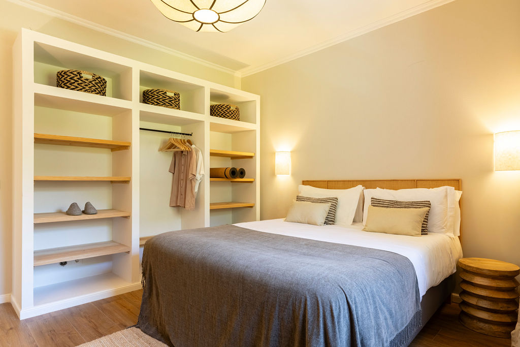 Bedroom one — built-in white shelving, wooden hangers and a grey wool throw