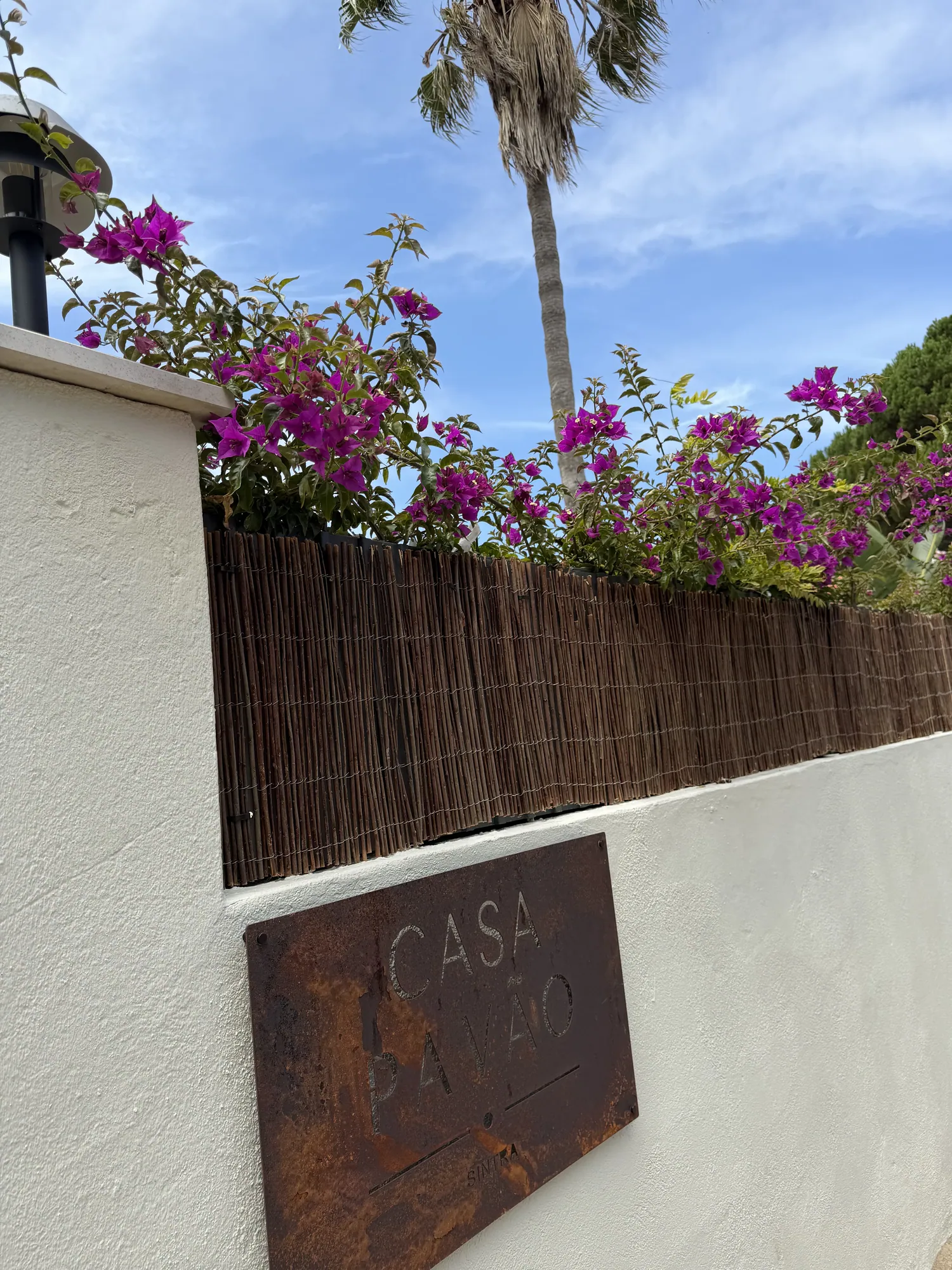 Casa Pavão sign on the white boundary wall beneath bougainvillea and a palm