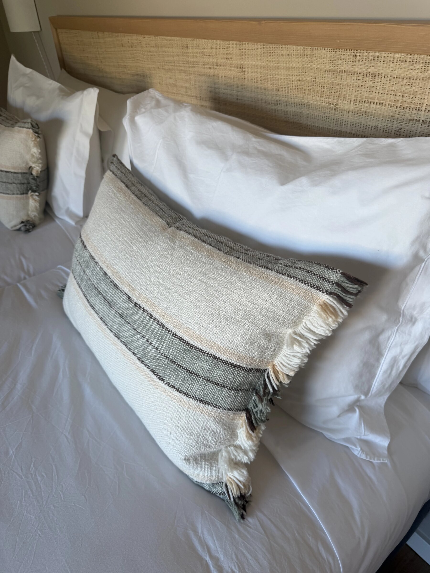 White bedding and a grey-striped linen cushion against a cane headboard