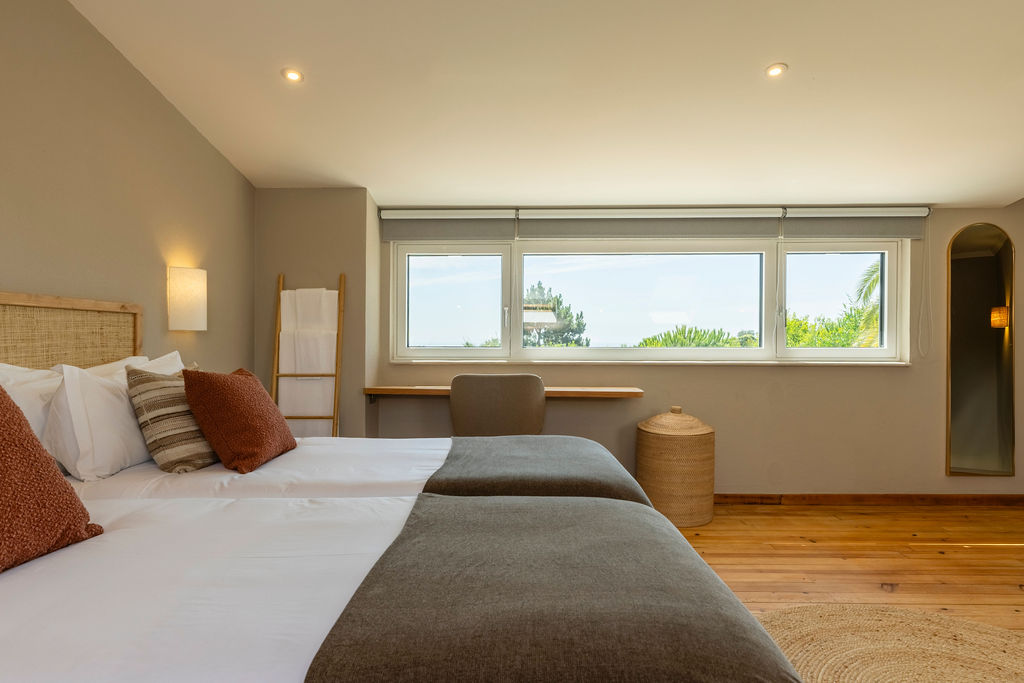 Bedroom three — rattan headboard, rust cushions and a long window onto the treetops