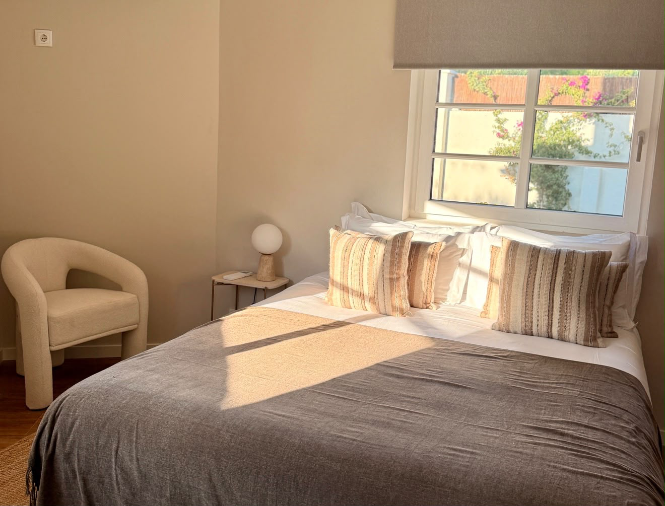 Double bed in soft morning light, striped cushions and a window onto flowering bougainvillea